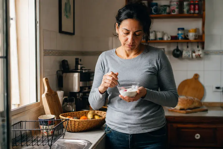 Mulher na cozinha a comer iogurte — pequeno-almoço sem pão